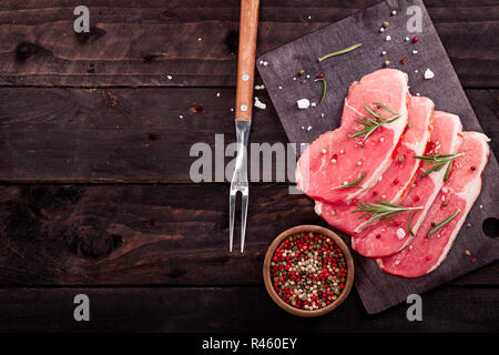 Raw meat. Raw beef steak on a cutting board with rosemary and spices on a black background with copy space. Stock Photo
