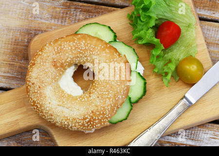 White sesame bagel with cream cheese and cucumber and cherry tomatoes on wooden board Stock Photo