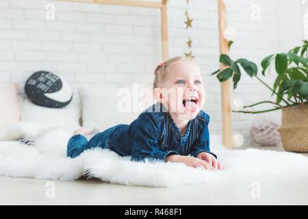 Cute little girl in blue denim overalls is lying on the bed. Stock Photo