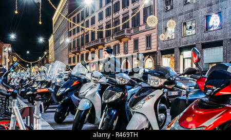 Rows of parked motor scooters in Milan at night. Vespas are an iconic Italian type of transport common in Italy Stock Photo