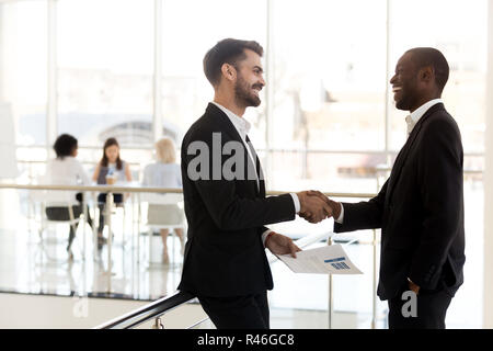 Diverse businessmen shaking hands introducing standing in modern Stock Photo
