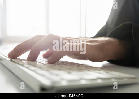 Low angle view of male businessman hand typing on white computer keyboard. Stock Photo