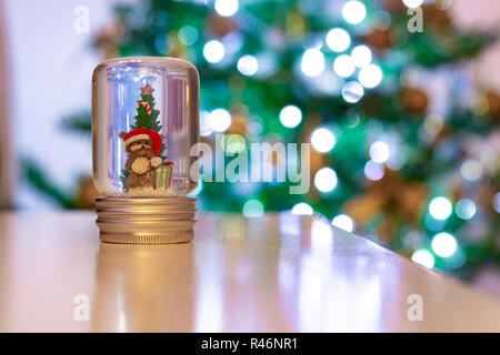 A bear in a snow globe in front of a defocused Christmas tree. Festive scene Stock Photo