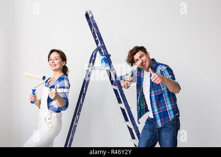 Repair, renovation and love couple concept - young man and woman in love and painting the wall, showing thumbs up Stock Photo