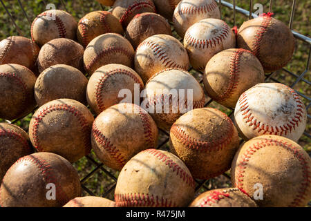 Close up of very used baseball balls in basket with grass background on sunny day. Stock Photo