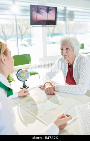 Travel agent picking up world tour for senior lady Stock Photo