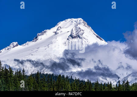 Mount Hood covered with snow with clouds from Frog Lake against a blue sky in early summer, Oregon, USA. Stock Photo