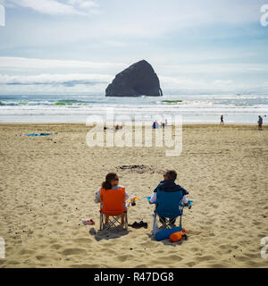Couple relaxing at Pacific City beach with Haystack Rock in the background on a nice day of summer, Cape Kiwanda, Oregon Coast, USA. Stock Photo