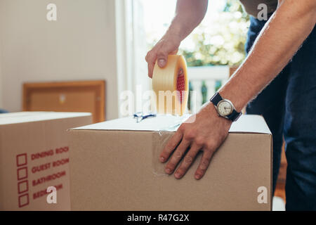 Man packing his household stuff in packing boxes and sealing them with adhesive tape. Stock Photo