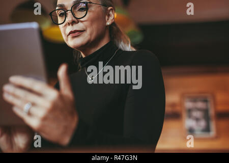 Senior woman wearing eyeglasses reading on digital tablet. Female at cafe using digital tablet. Stock Photo