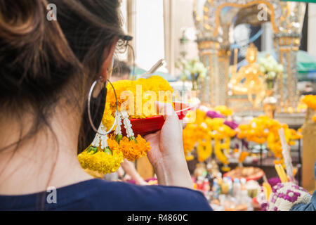 A woman make ceremonial offerings from floral garlands at the Erawan Shrine in Bangkok, Thailand. Stock Photo