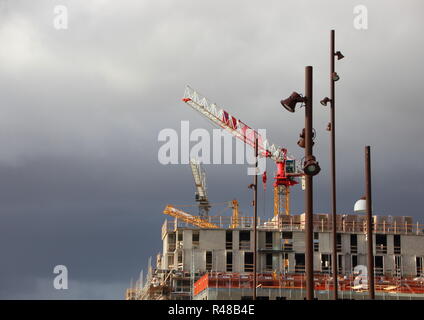 Cranes and Street Lamps at Building Site with Dark Clouds Stock Photo