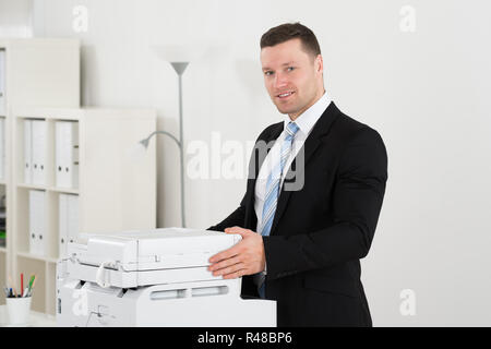 Confident Businessman Standing By Photocopy Machine Stock Photo