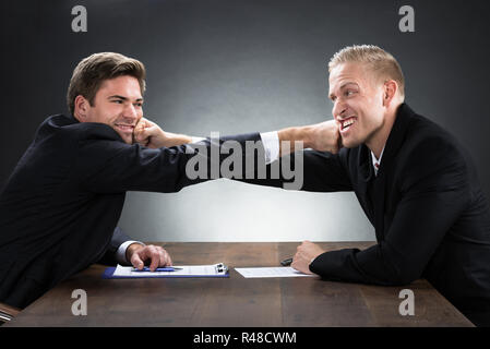 Young Businessmen Fighting At Wooden Desk Stock Photo