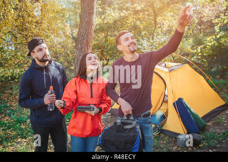 Excited young people look up. Woman holds remote control in hands. Guy on left has bottle of water. Man on right points up. Stock Photo