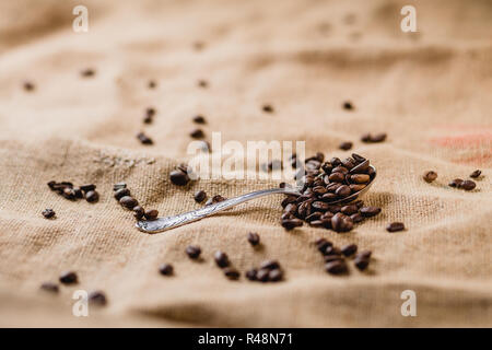 Coffee beans on a silver spoon lying on a brown, structured background, sprinkled with more coffee beans Stock Photo