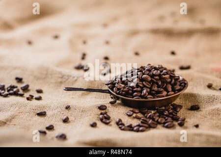 Coffee beans in a little pot lying on a brown, structured background, sprinkled with more coffee beans Stock Photo