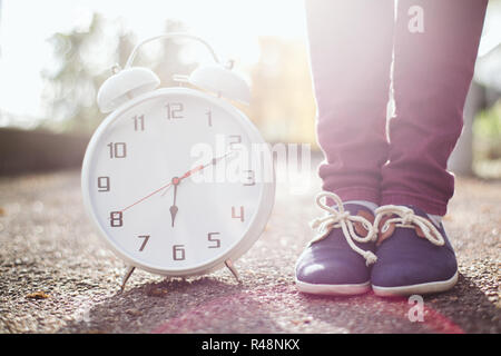 A woman standing next to a clock at sunset Stock Photo