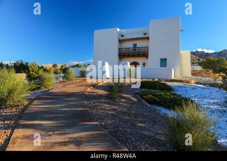 Traditional American southwest adobe house in the desert with snow and a sidewalk in New Mexico with blue sky Stock Photo