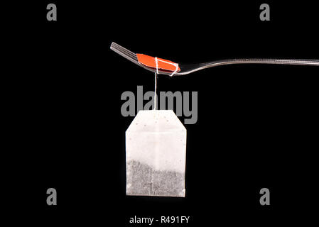 Bag of tea hanging on a fork isolated on a black background Stock Photo