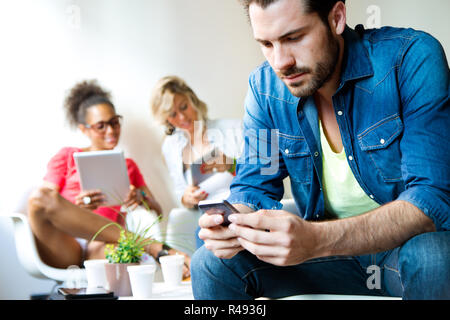 Young business man using his mobile phone, in the background business woman's use tablet. Stock Photo