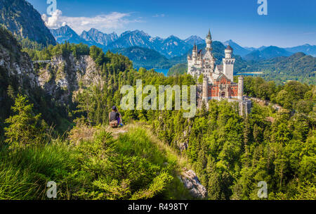 Classic view of famous Neuschwanstein Castle with male tourist enjoying the view from a steep cliff, Füssen, Bavaria, Germany Stock Photo