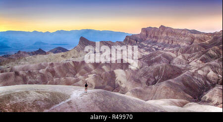 Panoramic view of man enjoying sunset at famous Zabriskie Point in beautiful golden evening light in summer, Death Valley National Park, California