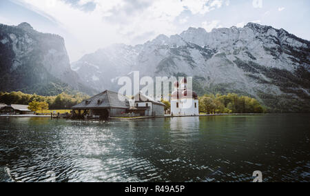 Classic panoramic view of Lake Konigssee with world famous Sankt Bartholomae pilgrimage church and Watzmann mountain in beautiful golden evening light Stock Photo