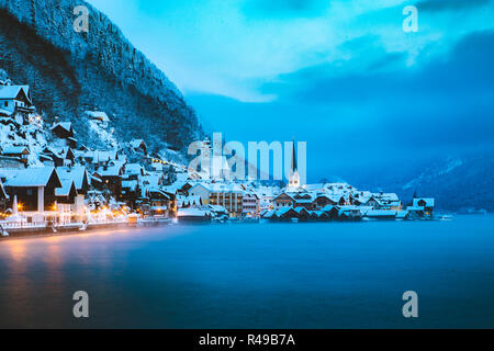 Panorama view of famous Hallstatt lakeside town in the Alps in mystic twilight during blue hour at dawn on a beautiful cold foggy day in winter, Salzk Stock Photo