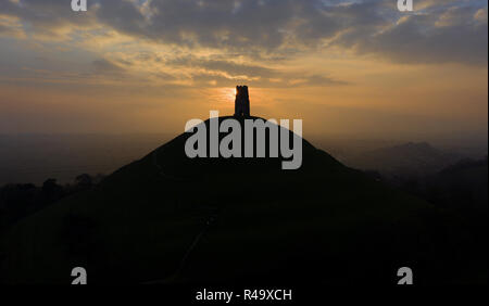 Glastonbury Tor, Somerset, UK. 26th November, 2018. The sun sets over the Glastonbury Tor in the English county of Somerset, topped by the roofless St Michael's Tower, a Grade I listed building. The whole site is managed by the National Trust, and has been designated a scheduled monument. The conical hill of clay and Blue Lias rises from the Somerset Levels. The Tor is mentioned in Celtic Mythology, particularly in myths linked to King Arthur, and has a number of other enduring mythological and spiritual associations Credit: David Bagnall/Alamy Live News Stock Photo