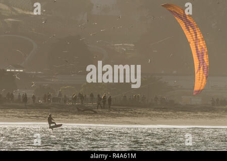 A kite boarder speeds past a beach in the late evening in San Francisco, the light catches the parachute. Stock Photo