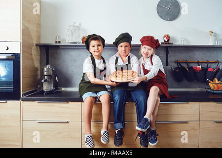 A group of children in a cook suit with pizza in the kitchen Stock Photo