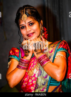 Bride Disha Sivarajah smiles and rests both mehndi-painted hands under her chin while getting ready for her Tamil Hindu wedding in Gustorf, a district of Grevenbroich, Germany. She wears a gold forehead pendant, a nose ring, red blossoms in her hair and tightly stacked bangles on both wrists. The couple is married later the same day at the Sivan temple of the Hindu Tamil Kultural Center in Dortmund-Hombruch. Stock Photo