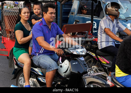 Couple with child on scooter in busy traffic on the riverfront at sunset. Preah Sisowath Quay, city centre, Phnom Penh, Cambodia Stock Photo