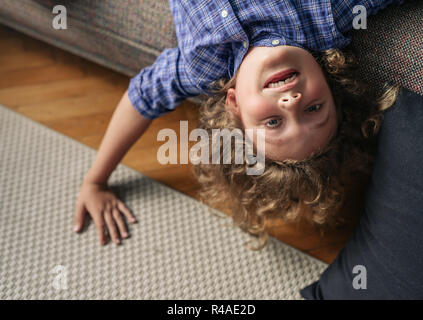 Little boy hanging upside down from his living room sofa Stock Photo