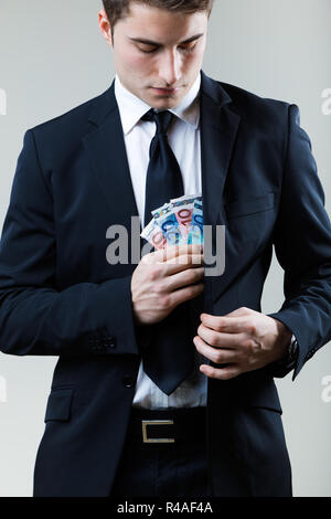 Young man in formalwear putting money in his pocket. Stock Photo