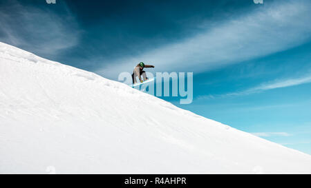 Active man on snowboard in snowy mountains over blue sky background, happy healthy lifestyle, extreme winter vacation Stock Photo