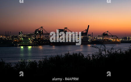 Silhouette of cranes and lights along the waterside of Eurpoort, near Rotterdam, The Netherlands. The twilight colors serve as a beautiful background. Stock Photo
