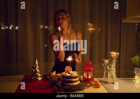 Young woman lighting a Sparkler in the cake at night at Christmas time Stock Photo