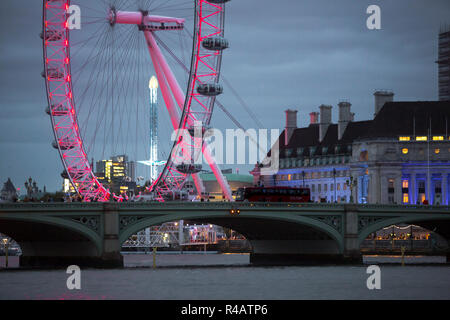 View of the Lodoon eye wheel on the banks of the River Thames in London illumintaed by red lights and set against a deep blue twilight sky with cloud in the autumn evening. Stock Photo