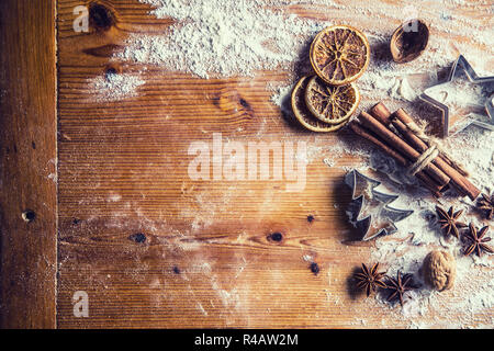 Top of view bakery table full of christmas aromatic ingredients star anise cinnamon dried orange flour cookery book and cookie cutters. Stock Photo