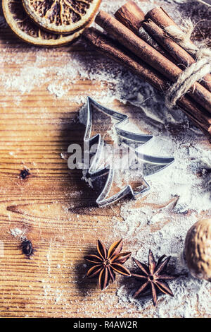 Top of view bakery table full of christmas aromatic ingredients star anise cinnamon dried orange flour cookery book and cookie cutters. Stock Photo