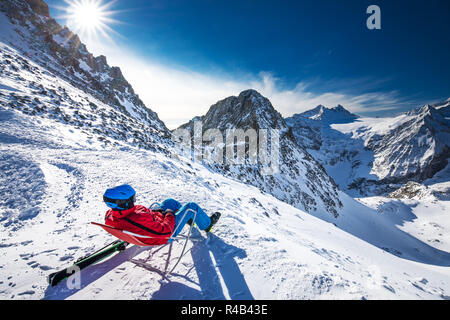 Young happy attractive skier sitting on the top of mountains enjoying the view from Presena Glacier, Tonale, Italy. Stock Photo