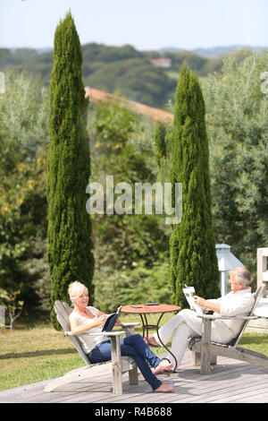 Senior couple in backyard reading book in deckchairs Stock Photo