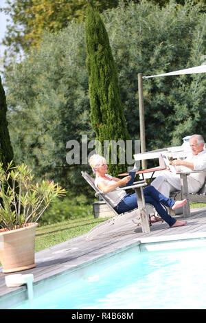 Senior couple in backyard reading book in deckchairs Stock Photo