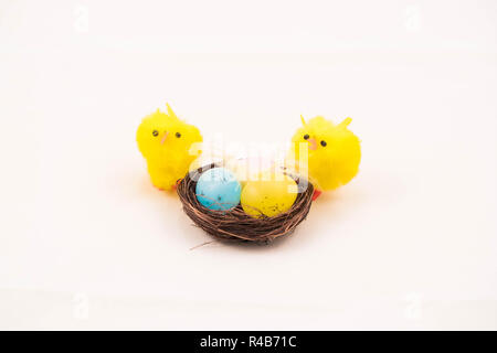 Easter fluffy toy chicks on nest with three eggs against white background. Stock Photo
