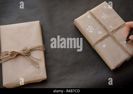 Woman drawing Snowflakes on paper package Christmas box Gift on black background. Female hands painting on Presents for winter Holidays. Christmas, Ne Stock Photo
