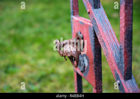 wrought iron handle at an open old garden gate with worn red color, copy space, close up with selected focus, narrow depth of field Stock Photo