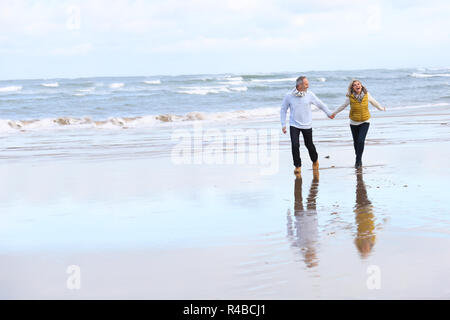Senior couple running on the beach in winter time Stock Photo