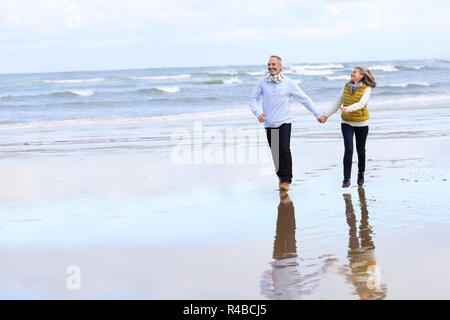 Senior couple running on the beach in winter time Stock Photo